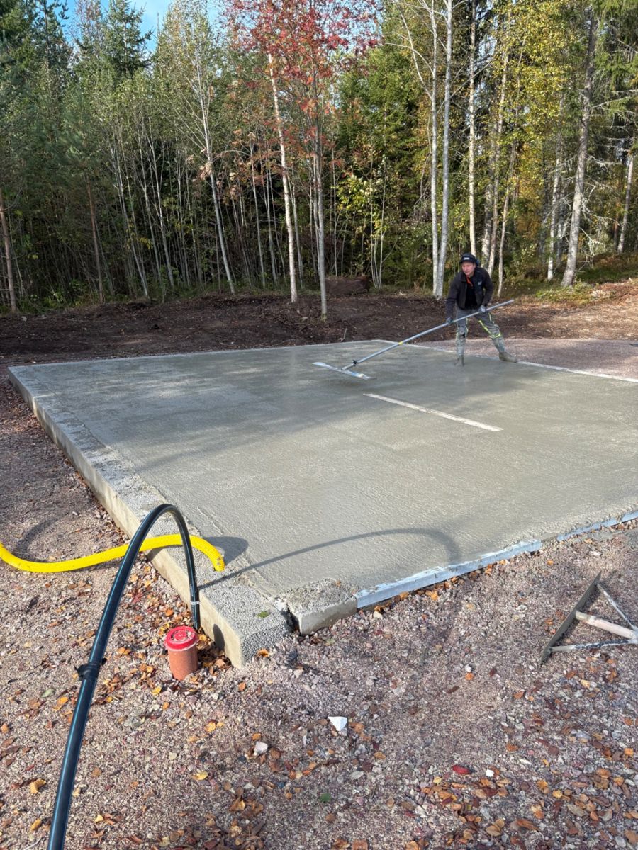 Arbetare jämnar ut nygjuten betongplatta med sloda intill skog