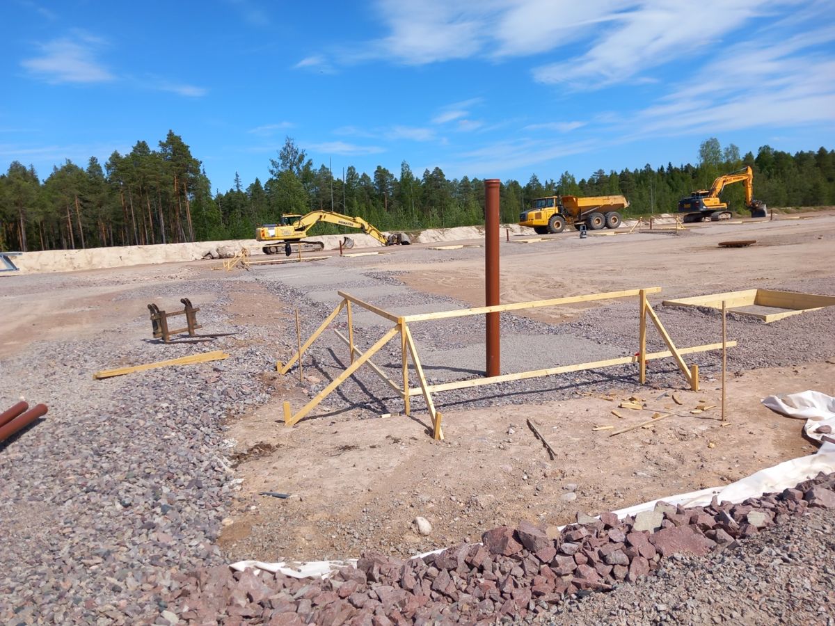 Schaktad och makadamerad tomt med utsättningsgalgar och markrör framför barrskog
