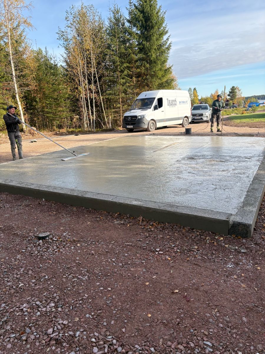 Hantverkare slutar av en nygjuten betongplatta medan en bil med Trapps-logotyp står parkerad intill