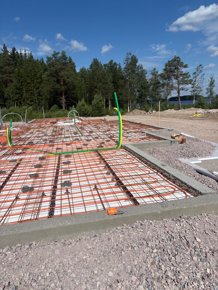 Förberedd betongplatta med cellplast, golvvärmeslingor, armering och skyddsrör vid en sjö